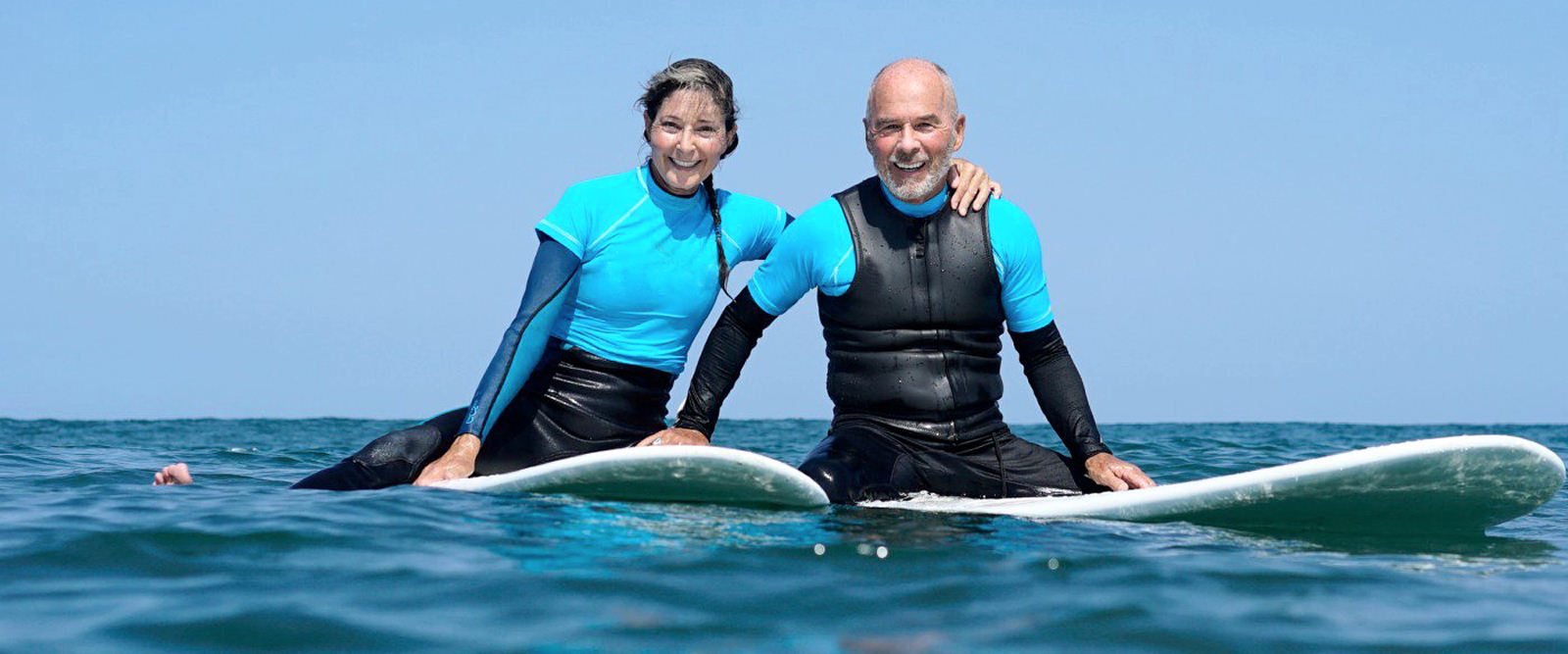 Surfing couple in wetsuits on rented surfboards